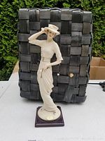 Full view of the 13-inch tall ivory resin figurine of a woman wearing a vintage dress and hat, on a dark wood base.