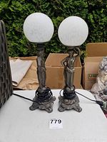Pair of Greek metal body lamps with glass globes on a table, showing full height and base design.