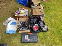 Overall photo showing boxes containing assorted tools, hardware, electrical parts, drawer pulls, and a case with the drill bit set.