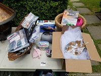 Photo showing hair extensions, eyelash sets in plastic packages on bent wood basket. Wicker basket on the side. Assorted items packed on table.