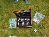 Full view of wooden chest open next to plastic bags containing additional flatware pieces.