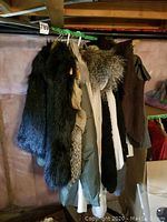 Photo showing a mix of fur vests and coats hanging on a wooden rack, featuring dark and multi-tone furs.