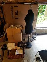 Overview of lot showing dressmaker's stand, box of hangers and wicker basket with fabric items and dust bags