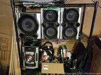 Overall photo showing the Sony stereo system components on shelving rack, including subwoofer, two speakers, stereo unit, headphones, cables, and video game cases on lower shelves.
