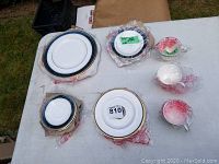 Various pieces of Royal Doulton china laid out on a white surface, including plates, saucers, and teacups, some wrapped in protective tissue.