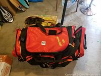 Red and black hockey bag with multiple handles and compartments on floor