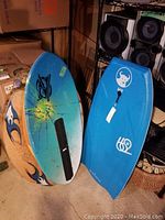 Three boards including a blue and teal boogie board, blue boogie board, and orange flame skim board leaning against a wall.