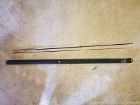 Two-piece fishing rod and black carrying case laid out on carpeted floor showing rod sections and case length.