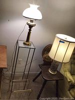 Brass base lamp, tall metal and glass table, and magazine rack shown together in room.