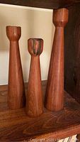 Set of three wooden candleholders of varying heights on a wooden shelf