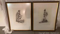 Pair of framed etchings, each 18x22 inches, showing elderly woman and man in detailed line art, framed in gold.