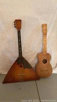 Balalaika and ukulele shown standing side by side on neutral backdrop.