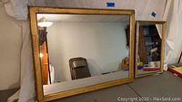 Photo showing a large gilt framed wall mirror measuring approximately 24x19 inches, with classic gold frame and clear glass.