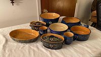 Image showing various pieces of the pottery set including two coffee cups, multiple bowls, and serving dishes with blue and white floral designs.