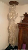 Full view of tall capiz shell chandelier hanging from wooden ceiling mount against corner wall.