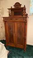 Front view of antique Victorian wardrobe showing two-door design, brass handles, carved details, and turned columns.