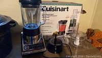 Cuisinart Power Blend Duet blender and food processor with accessories displayed on a table with original box in background.