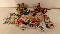 Vintage German Christmas ornaments spread on a white cloth including Santa, cardinal bird on sled, elves, angels, and toys.