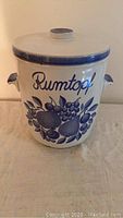 Front view of ceramic Rumtopf pot with blue fruit and floral design and lid with knob handle.