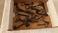 Photo showing a group of about 17 antique skeleton keys in an open box with a brown base. Keys vary in size and style, some are rusted and aged.