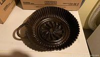 Top-down photo showing cast iron Bundt pan with ridged edges, decorative center, and attached handle.