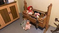 Wooden cradle with two dolls inside and two dolls sitting next to it on the floor.
