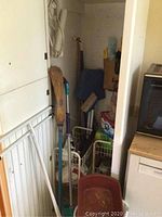 General view of cleaning supplies including brooms, mops, buckets, dustpans, stored in a small utility space.