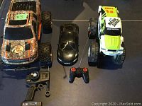 Top view showing three toy vehicles and two remote control devices, two large monster trucks and one smaller black car.