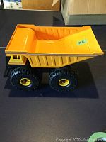 Side view of the sturdy orange toy dump truck on a dark surface showing full body and wheels.