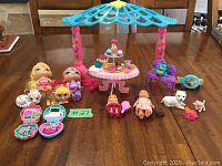 Image showing a collection of assorted girl toys featuring Polly Pocket style compact playsets, several small dolls, animal figures, and a pink/purple canopy café table with miniature tea set and pastries