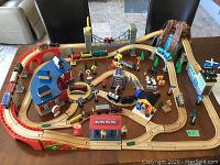 Overview of assembled wooden train layout with tracks, locomotives, cars, buildings and accessories on table