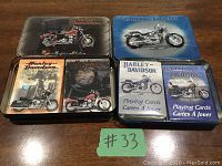 Four Harley Davidson playing card collector tins on wooden surface showing two unopened blue decks and two opened tins with various motorcycle art.