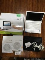 Overview of the Asus Eee PC mini laptop, original box, user manuals, software CDs, charger with cable, and soft carrying case on wooden surface.