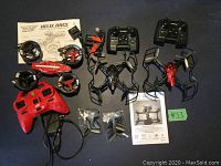 Photo shows all three drones with respective controllers, two drone instruction manuals, charging cables, and spare parts on a dark surface.