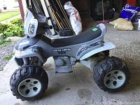 Side view of the gray and black child's ride-on ATV with Special Forces decals showing large plastic wheels and black seat