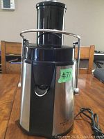 Sharper Image electric juicer front view on a wooden table showing stainless steel and black plastic body, safety locking arm, and feeding chute.