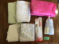 Five folded fitted crib sheets and an unopened bundle of baby washcloths alongside a Fisher-Price bottle brush in packaging on wooden surface