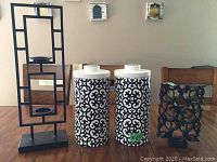 Full view of all four black and white decorative pieces including candle holder, two ceramic canisters, and composite design piece on wooden floor