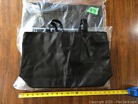 Front view of one black bag with handles, measuring tape below indicating approx 16 inches width