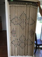 Full view of wooden bead curtain hanging from a black horizontal rod, showing the geometric pattern with bead strings.