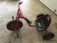 Side view of red reclining tricycle showing metal frame, black plastic seat and pedals.