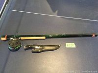 Full view of fly fishing rod with reel and filet cutter in sheath on a flat surface.