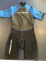 Front view of medium size Mica wetsuit, short sleeves and legs, black and blue color with logo on chest and thigh.