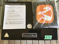 Top view of the BakerStone pizza oven showing the instruction manual, built-in thermometer, and protective cover in packaging.