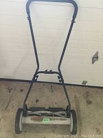 Front view of the push reel lawnmower showing the upright handlebar, two rear wheels, and the blade reel at the base.