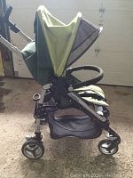 Side view of green Peg Perego stroller, showing the frame, wheels, seat, canopy, and storage basket below. The stroller has signs of wear including peeling.