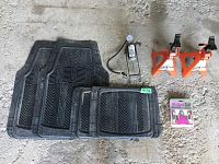 Photo showing set of four black rubber floor mats with textured tread pattern, two orange metal axle stands, and silver metal foot pump on rough concrete floor.