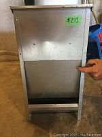 Front view of the metal dog food dispenser showing rectangular box with open feed area and mounting holes on back panel.