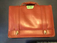 Front view of the brown soft leather briefcase with two gold-tone clasps and handle.