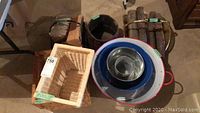 Photo showing a wood barrel, two wood log holders tied in small bundles, three wicker baskets of varying sizes, a large red and white metal bucket with two smaller galvanized metal buckets nested inside, and additional small containers on the floor.